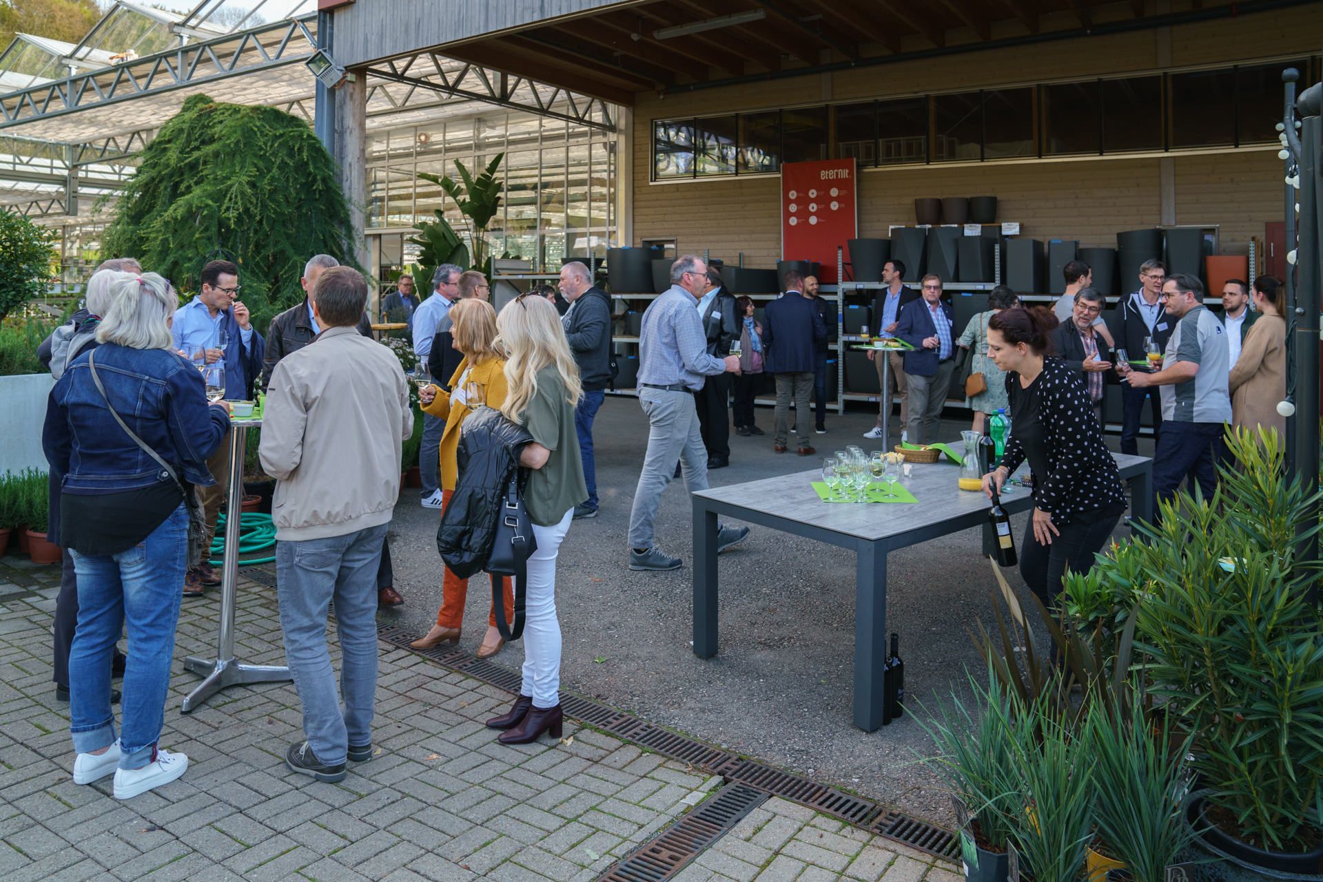 Eine Gruppe von Menschen steht in einem Gewächshaus um einen Tisch herum.