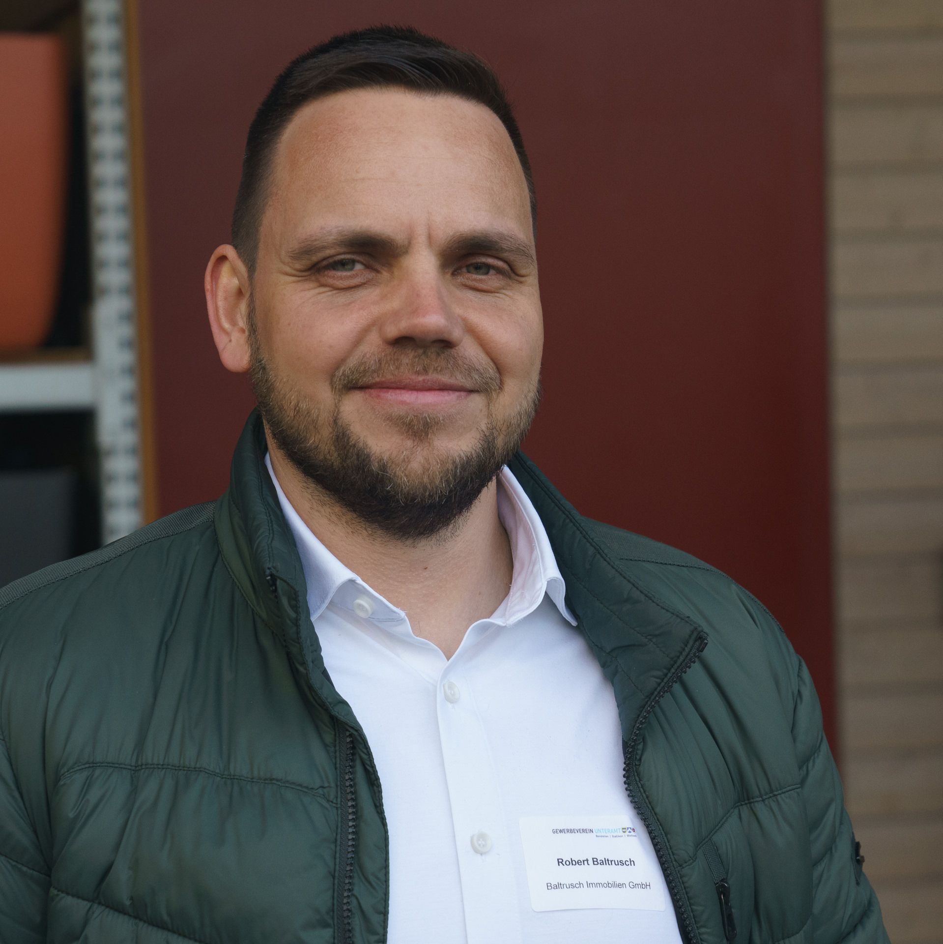 Ein Mann mit Bart trägt eine grüne Jacke und ein weißes Hemd