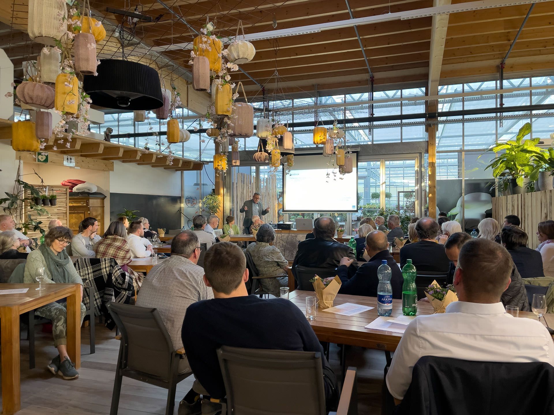 Eine Gruppe von Leuten sitzt an Tischen in einem Restaurant und sieht sich eine Präsentation an.