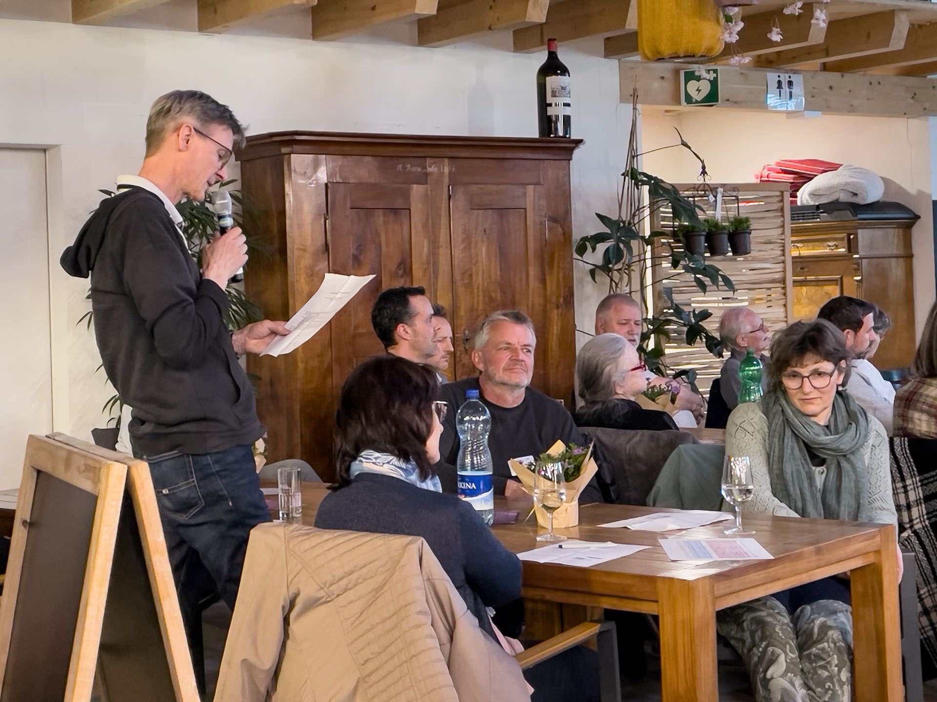 Ein Mann hält eine Rede vor einer Gruppe von Leuten, die an Tischen sitzen.
