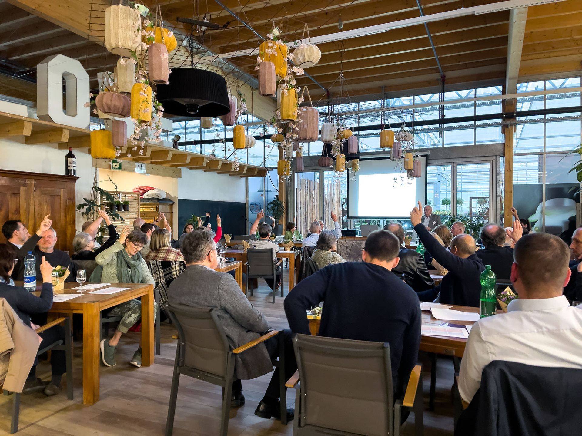 Eine Gruppe von Menschen sitzt in einem Restaurant an Tischen und hebt ihre Hände.