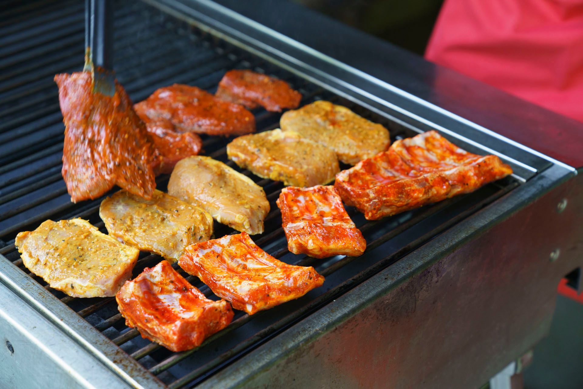 Eine Person grillt Fleisch mit einer Zange.