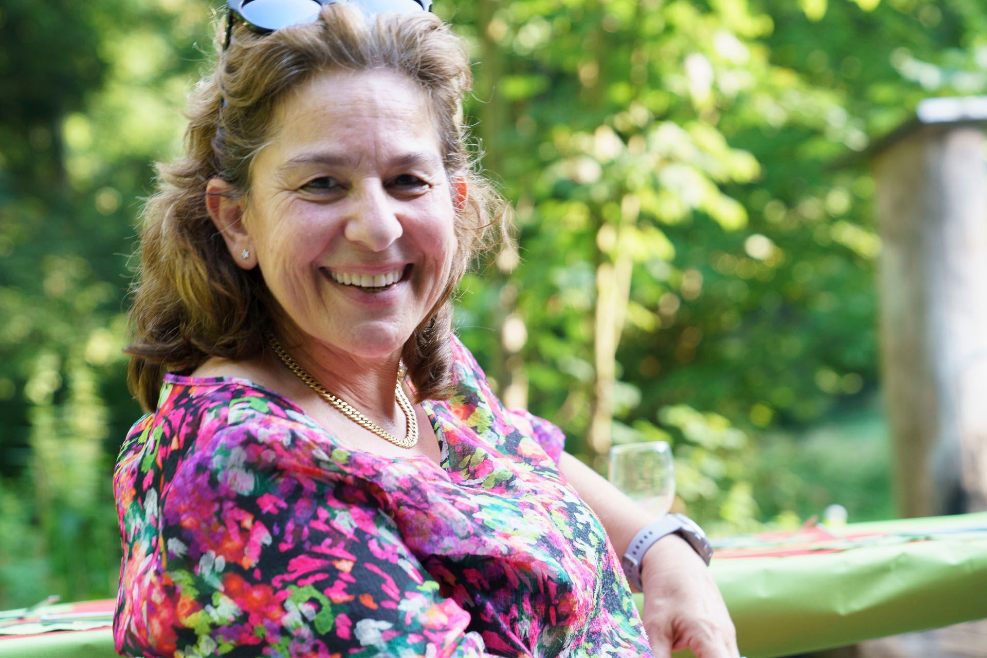 Eine Frau lächelt, während sie mit einem Glas Wein an einem Tisch sitzt.