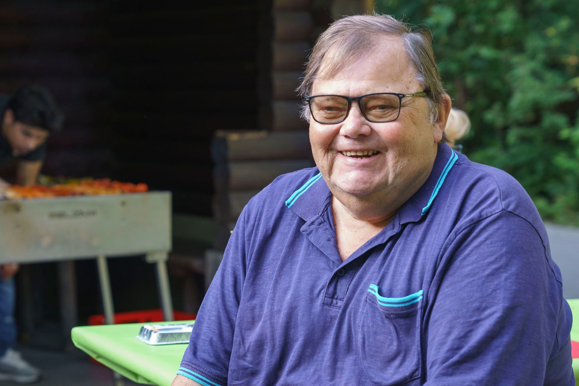 Ein Mann mit Brille sitzt an einem Tisch und lächelt.