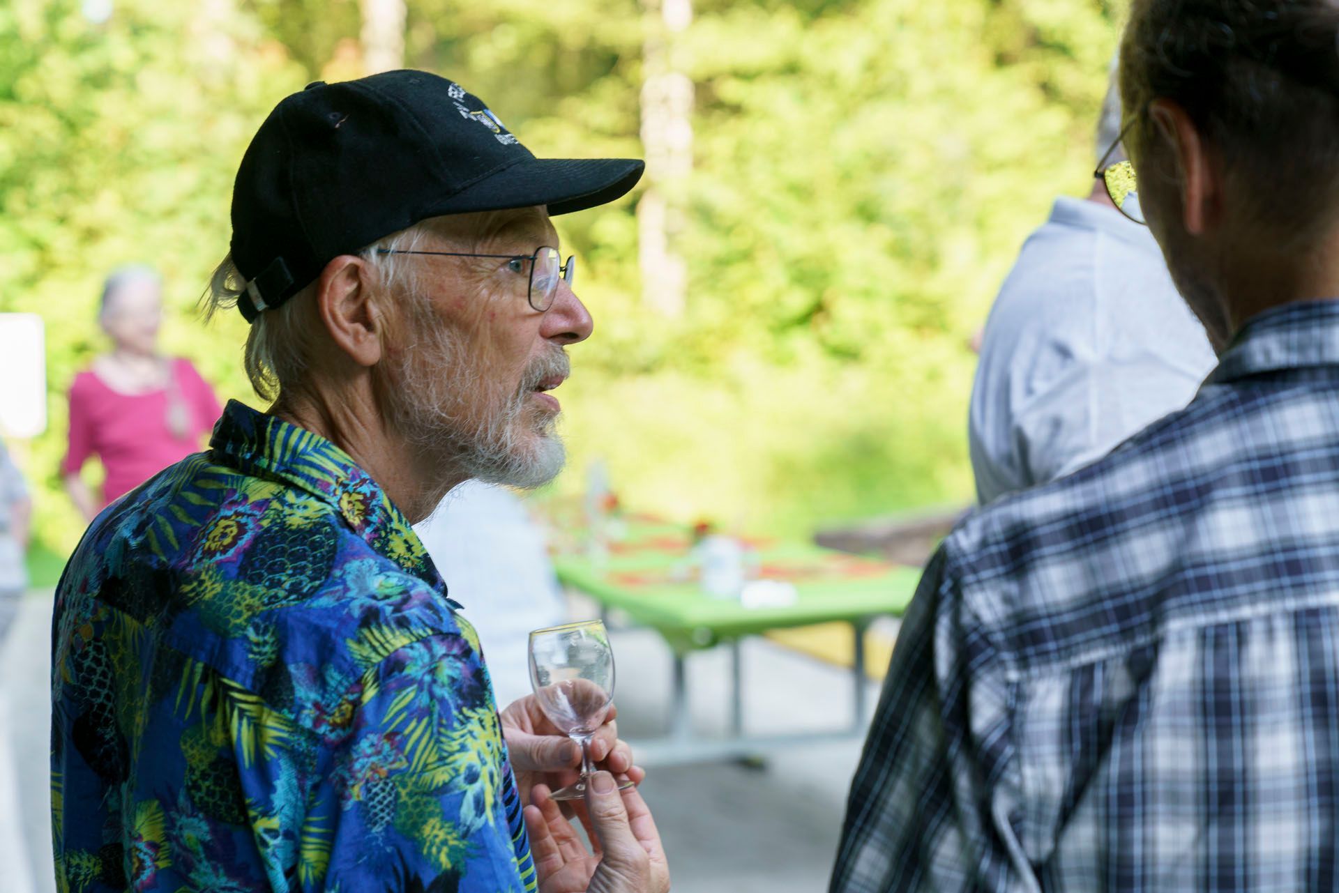 Ein Mann mit Bart hält ein Glas Wein und unterhält sich mit einem anderen Mann.