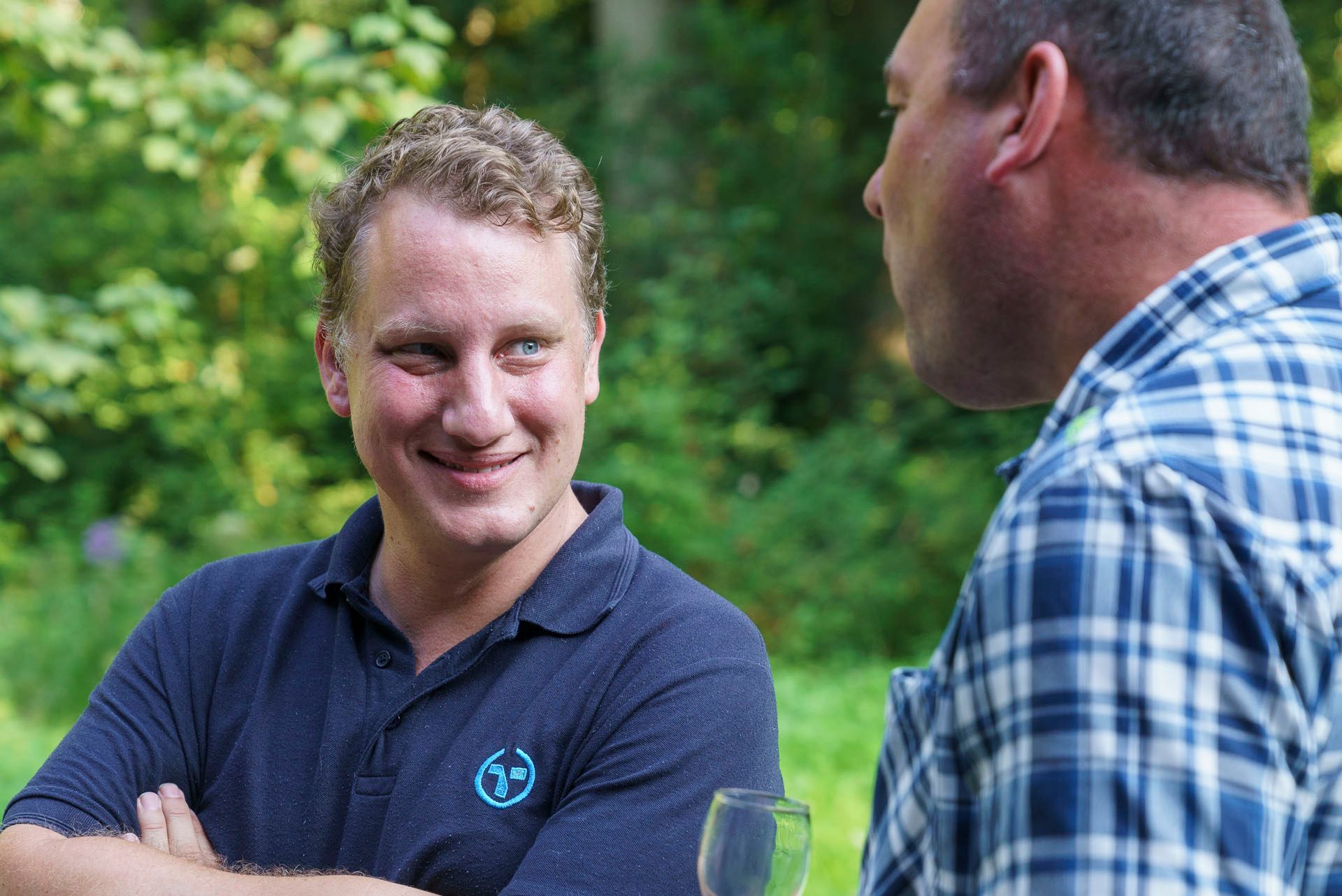 Zwei Männer stehen nebeneinander und unterhalten sich. Einer der Männer trägt ein kariertes Hemd.