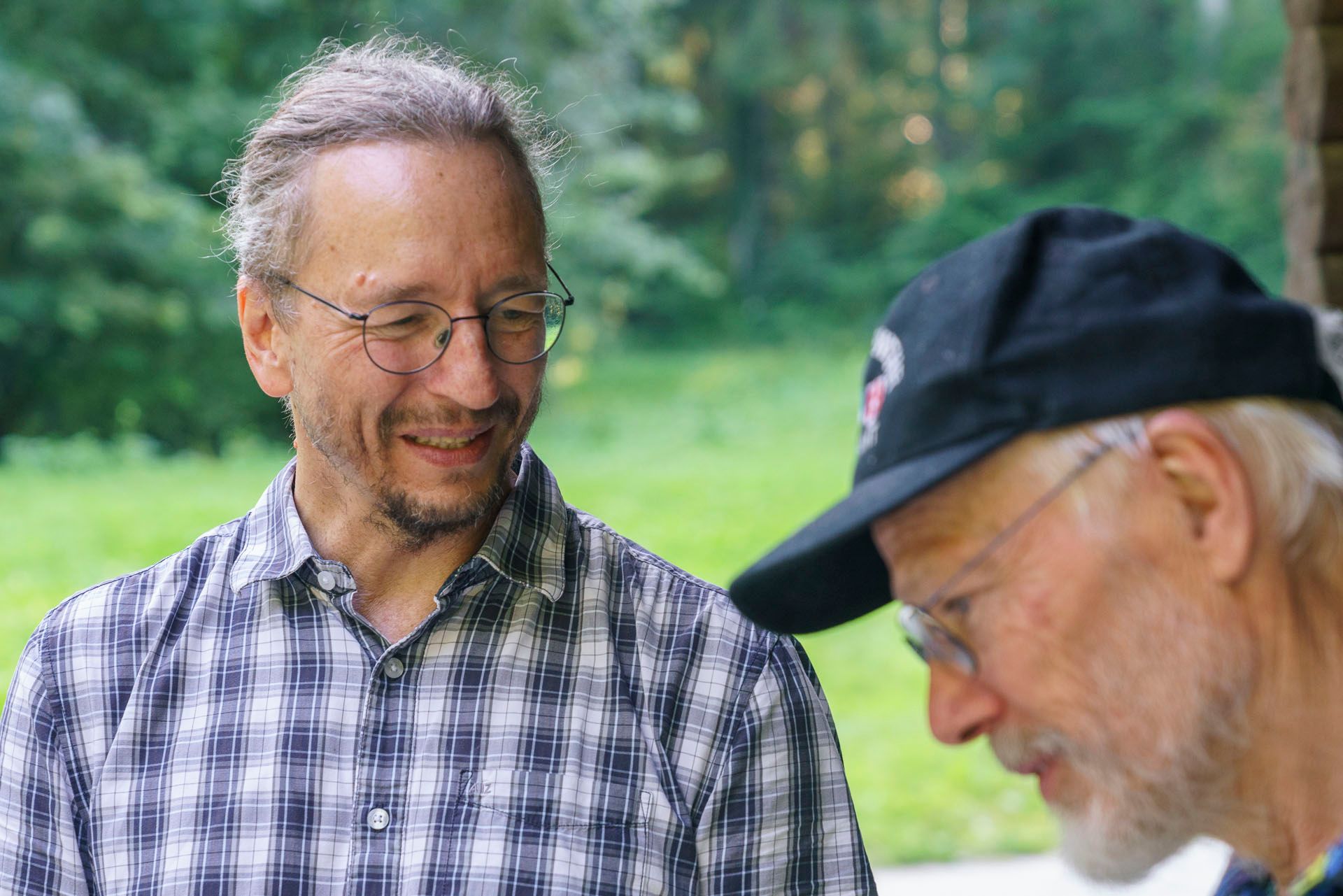 Ein Mann mit kariertem Hemd und schwarzem Hut spricht mit einem anderen Mann