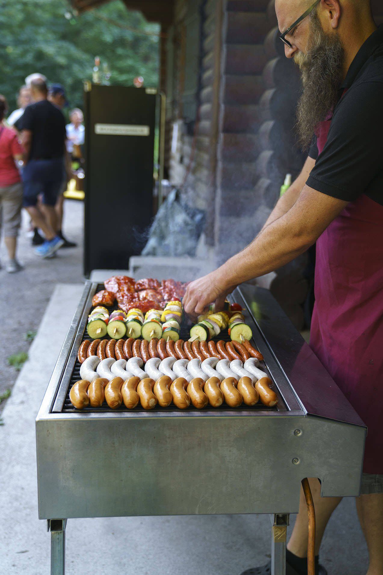 Ein Mann grillt Würstchen und Gemüse.