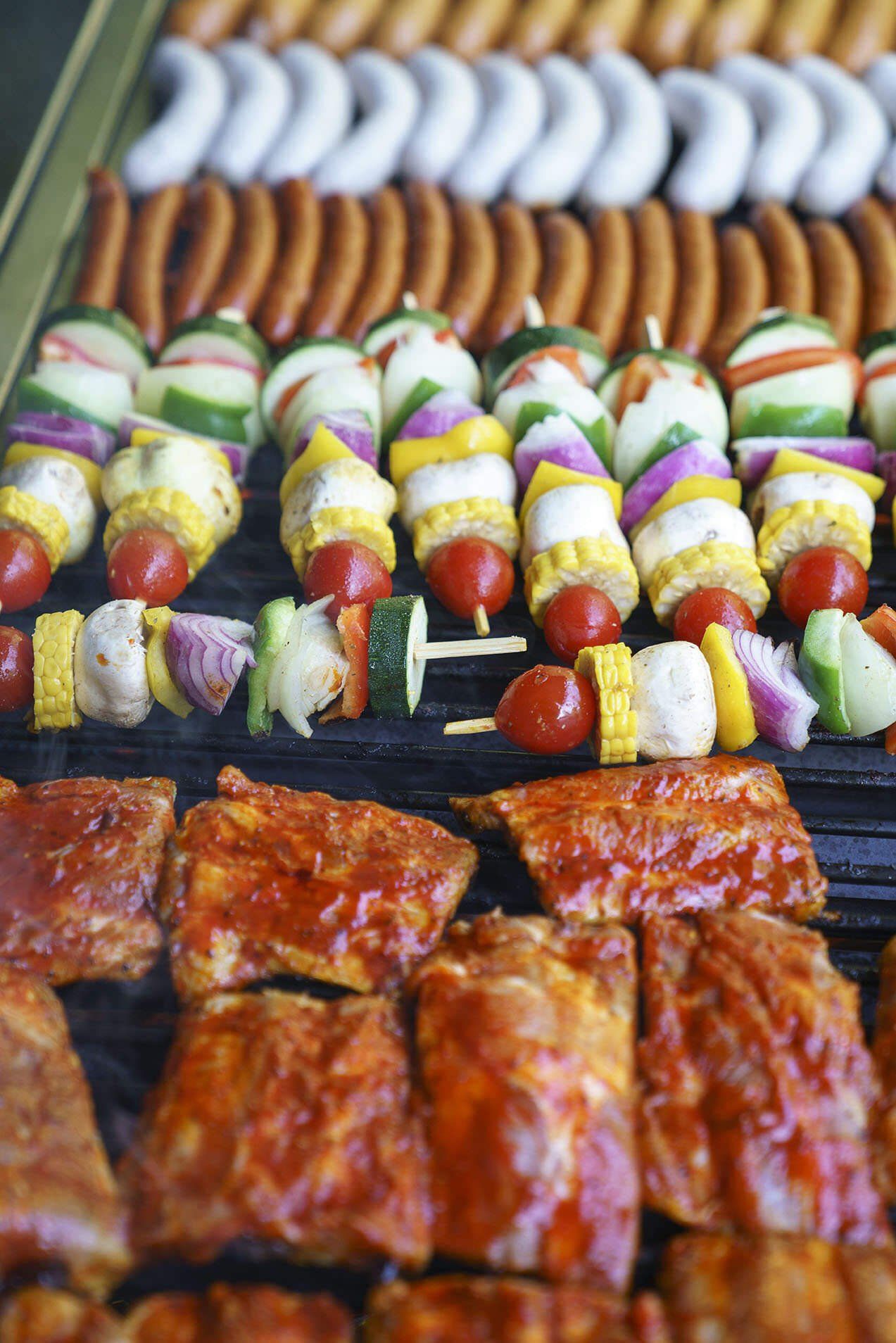 Ein Grill gefüllt mit Fleisch und Gemüse, darunter Rippchen und Spieße.