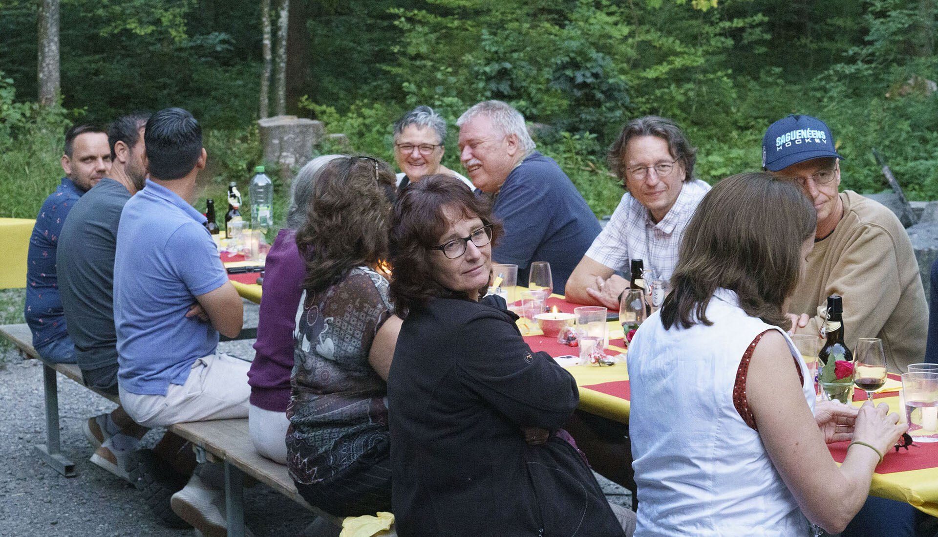 Eine Gruppe von Leuten sitzt an einem langen Tisch im Wald.