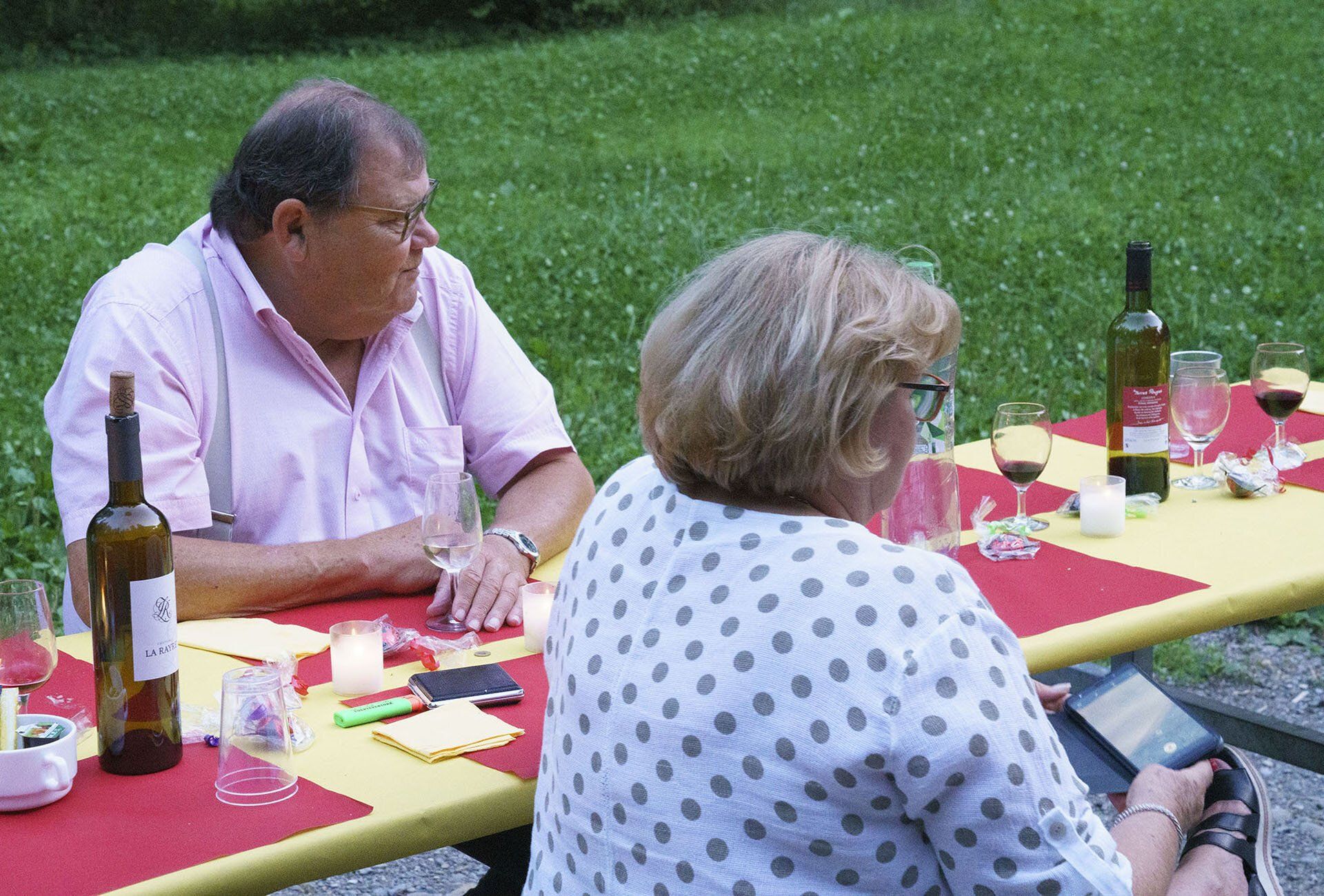 Ein Mann und eine Frau sitzen mit Weingläsern und einer Flasche Wein an einem Tisch.