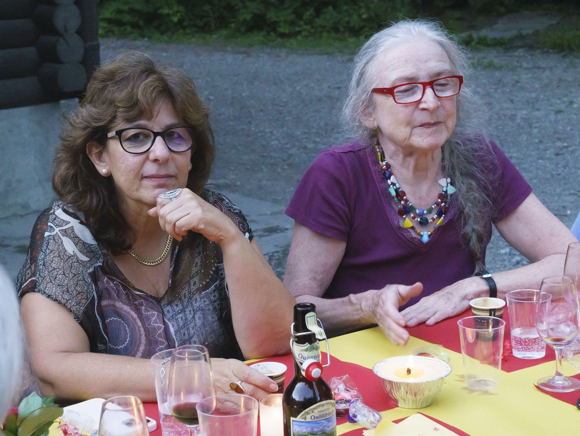 Zwei Frauen sitzen mit Weingläsern und Kerzen an einem Tisch.