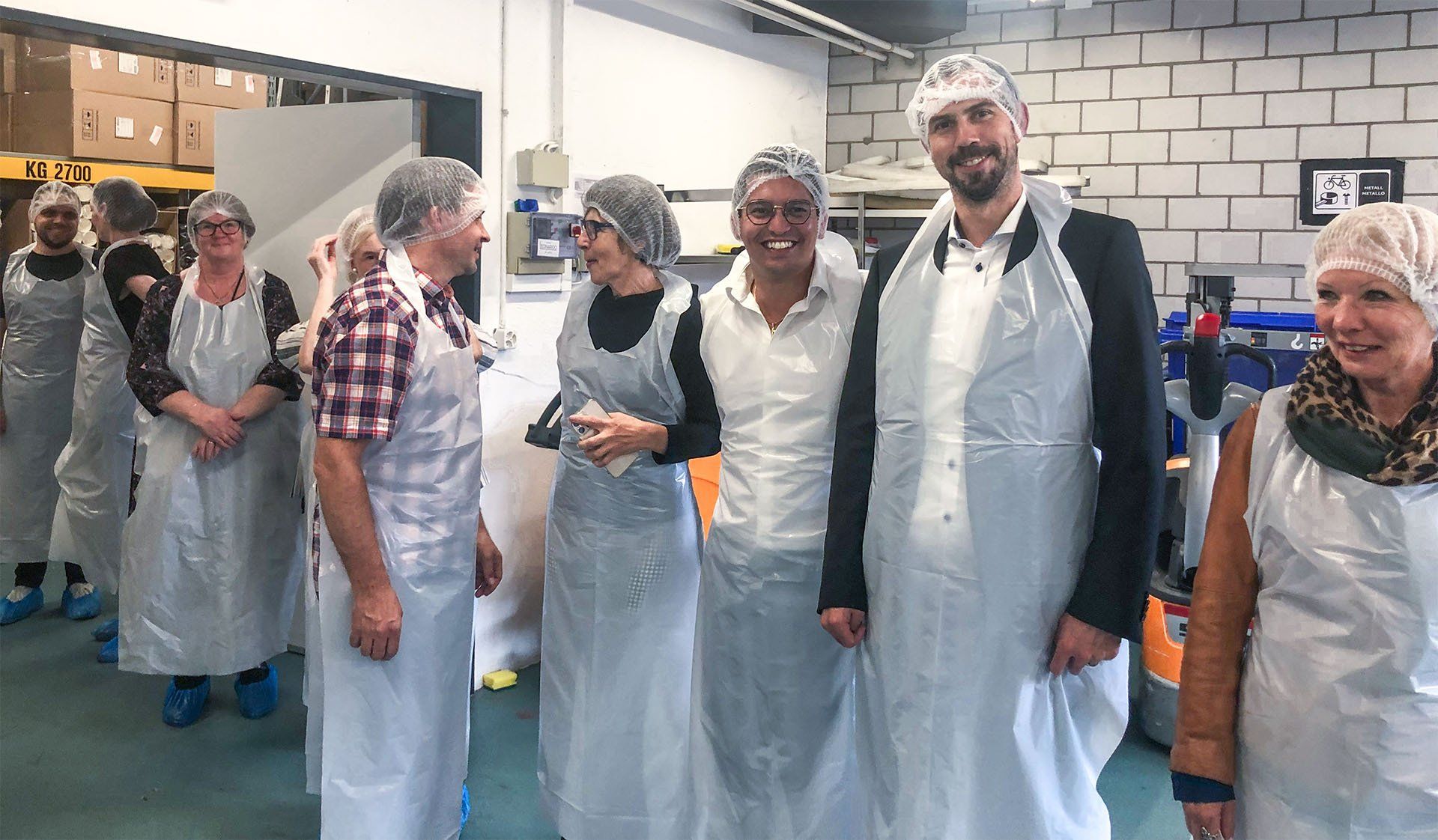 Eine Gruppe von Menschen mit weißen Schürzen und Plastikhüten steht in einem Raum.