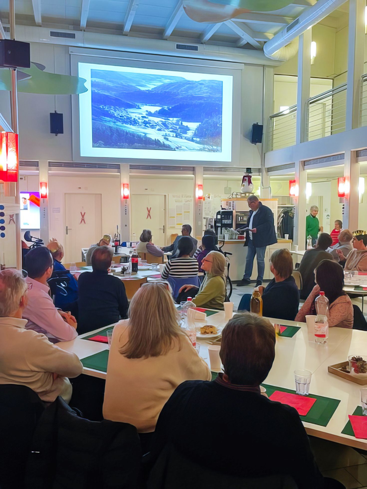 Eine Gruppe von Menschen sitzt an Tischen vor einer Projektionsleinwand.