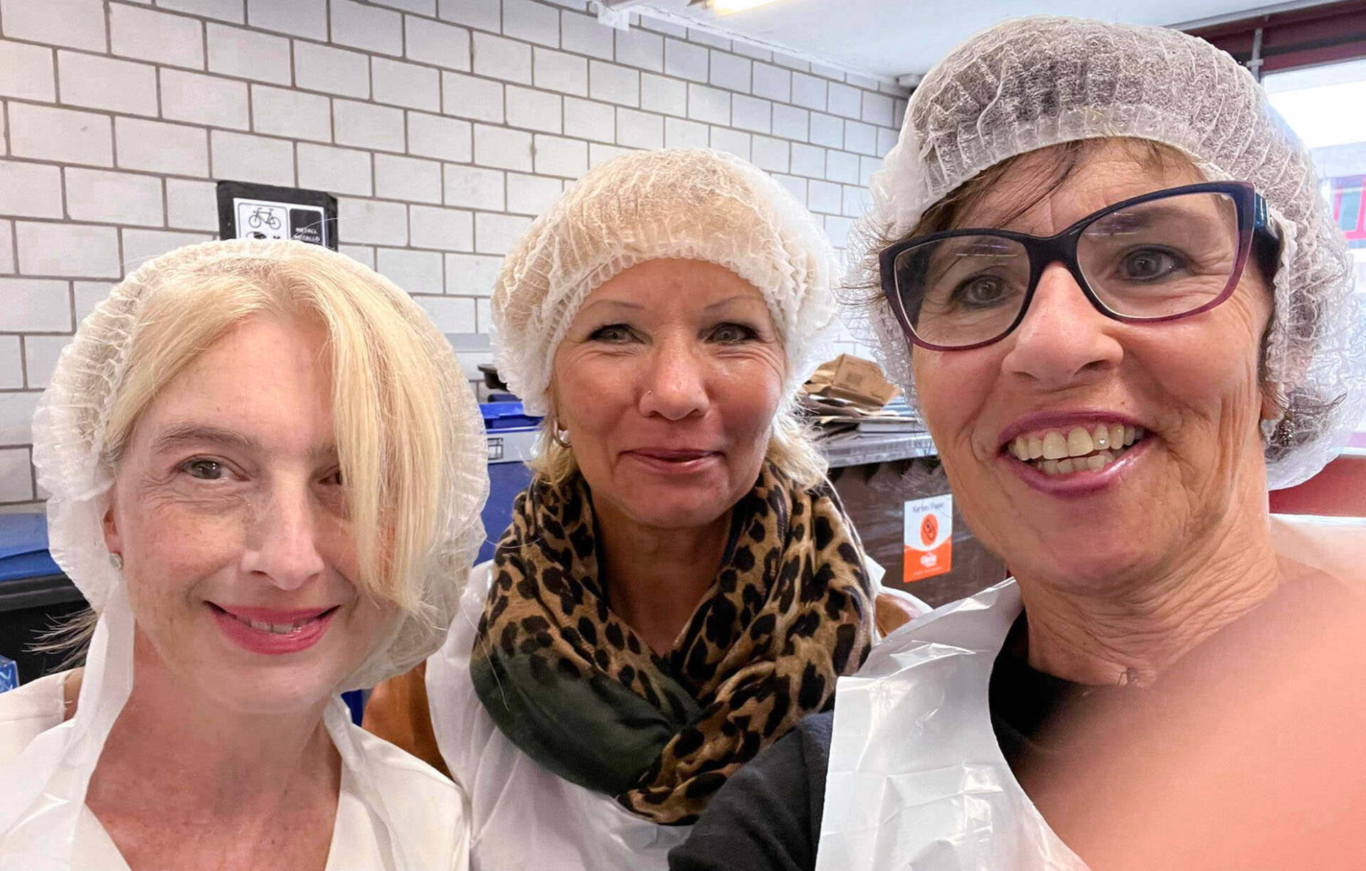 Drei Frauen mit Plastikhüten und Schürzen posieren für ein Foto.