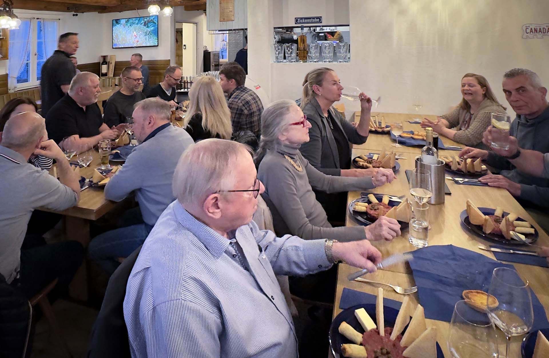 Eine Gruppe Leute sitzt an einem langen Tisch, isst und trinkt Wein.