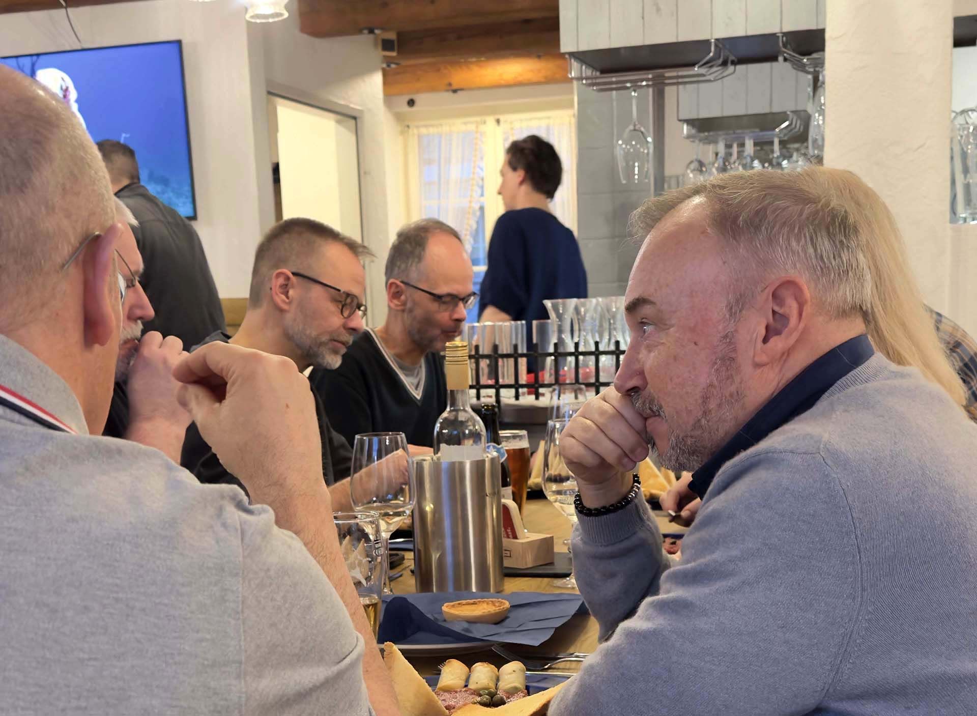 Eine Gruppe von Männern sitzt in einem Restaurant an einem Tisch und unterhält sich miteinander.