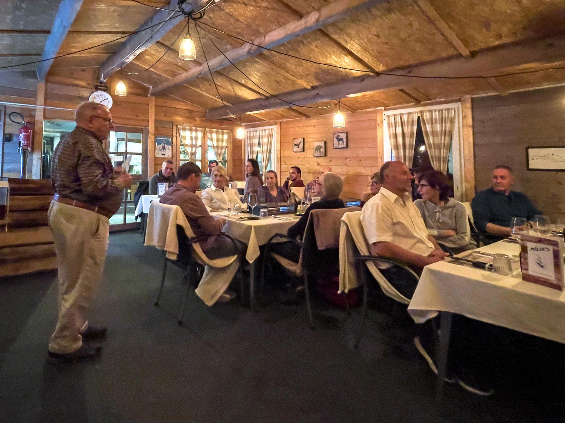 Ein Mann steht vor einer Gruppe von Leuten, die in einem Restaurant an Tischen sitzen.