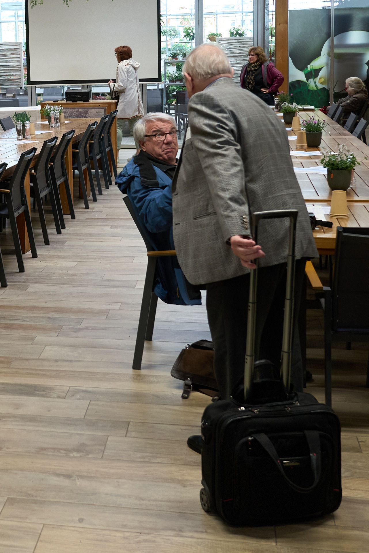 Zwei Männer stehen nebeneinander in einem Raum mit Tischen und Stühlen.