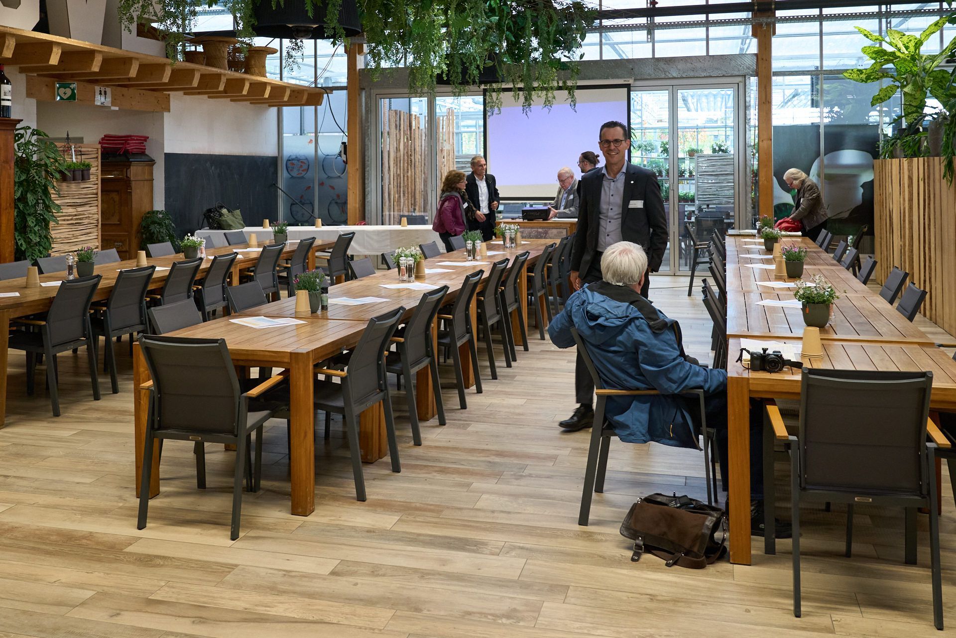 In einem Restaurant steht ein Mann neben einer Frau und sitzt an einem Tisch.