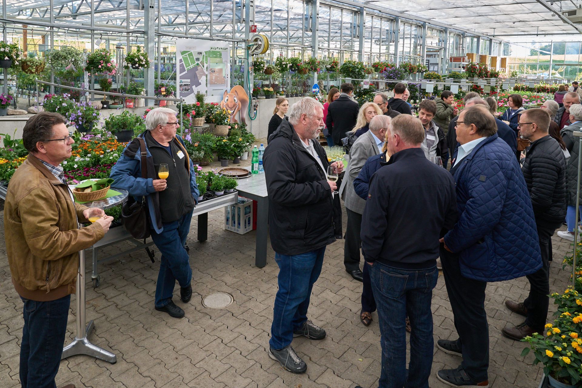 Eine Gruppe von Leuten steht in einem Gewächshaus und unterhält sich.