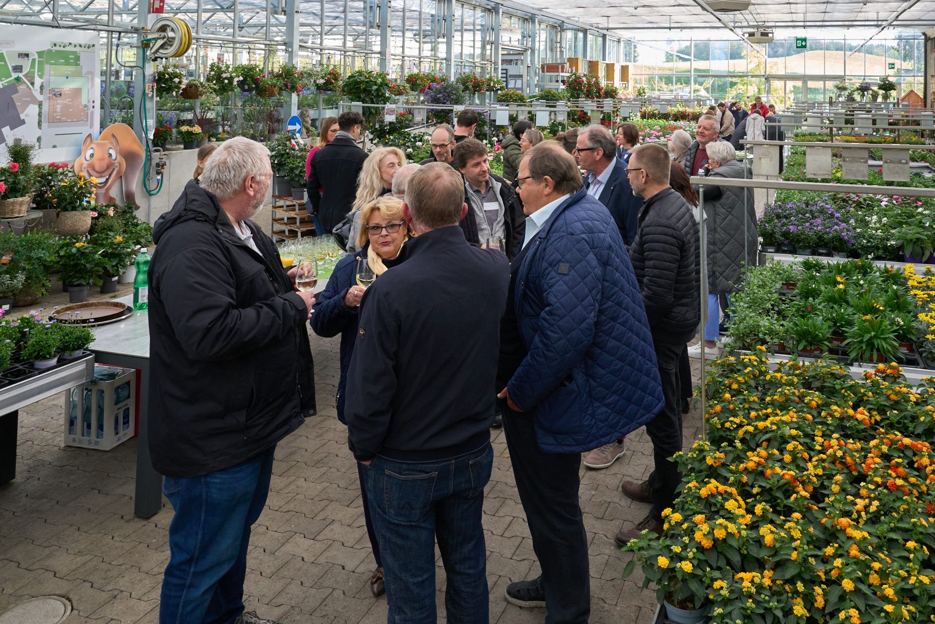 Eine Gruppe von Leuten steht in einem Gewächshaus und unterhält sich.