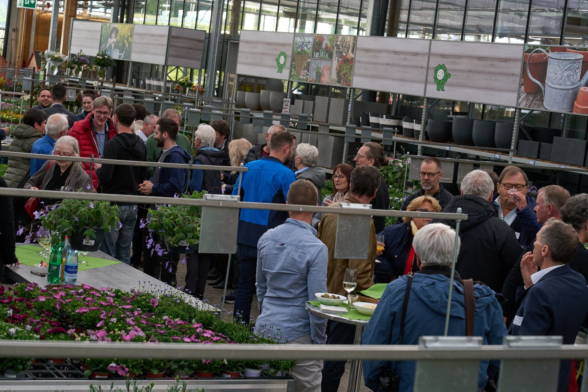 Eine Gruppe von Menschen steht in einem Gewächshaus um einen Tisch herum.