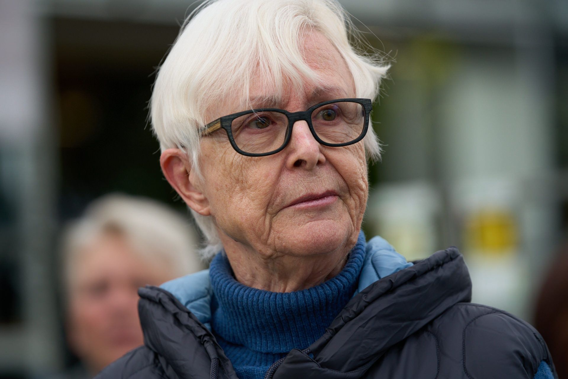 Eine Nahaufnahme einer Frau mit Brille und blauem Pullover.