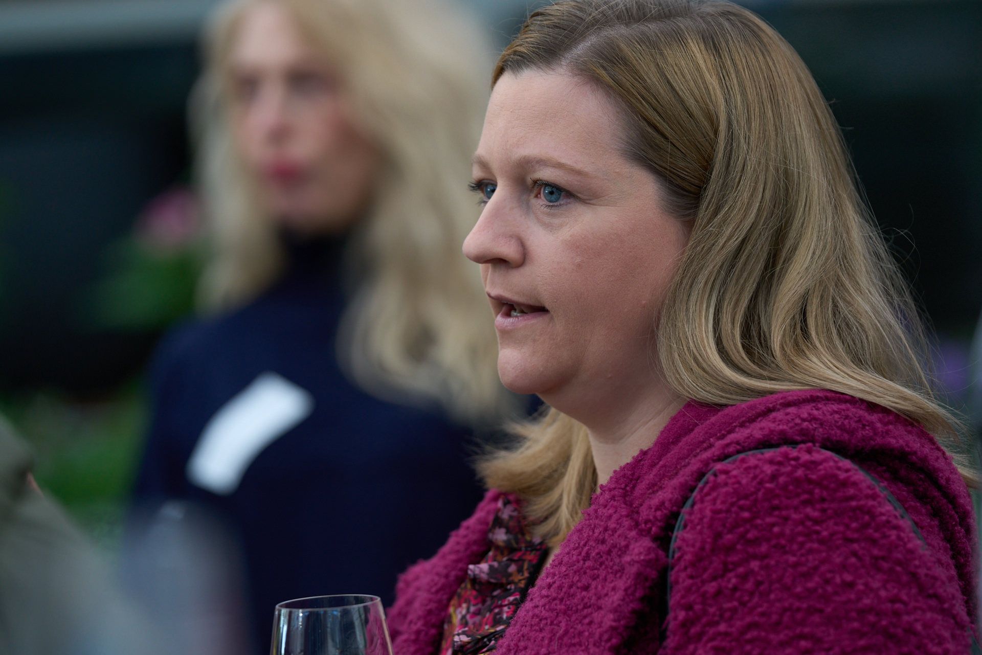 Eine Frau in einem rosa Mantel hält ein Glas Wein.