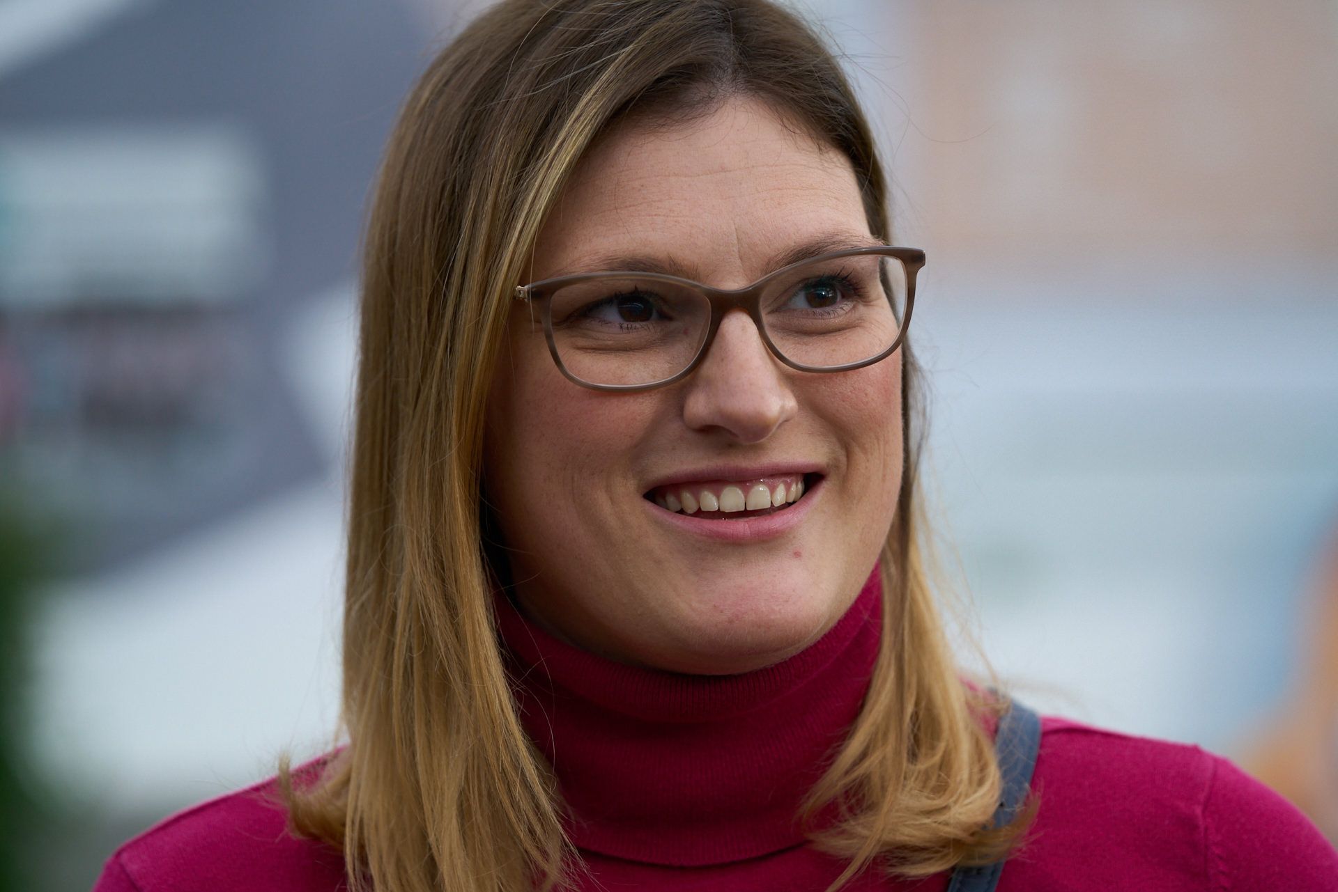 Eine Frau mit Brille und rotem Rollkragenpullover lächelt.