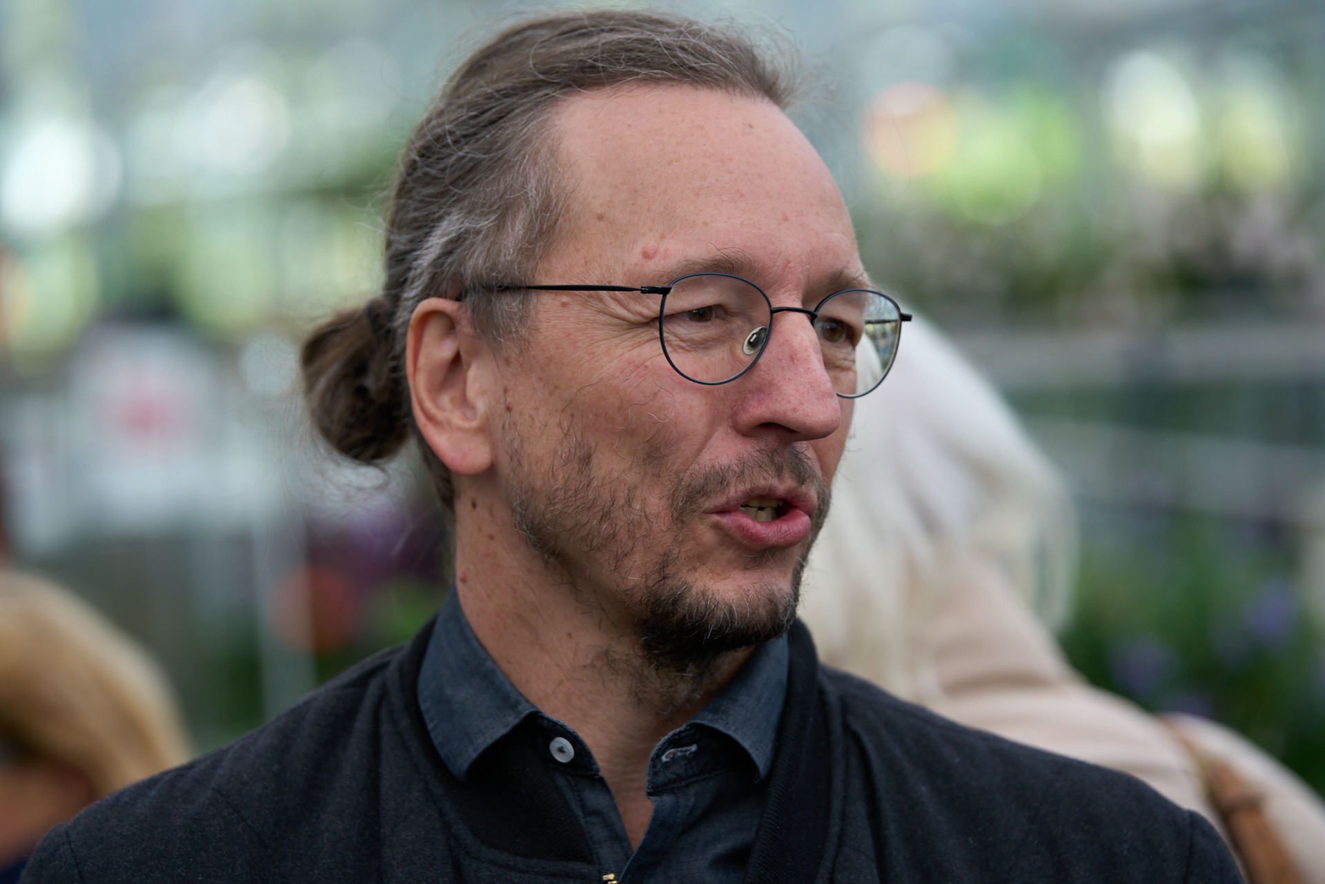 Ein Mann mit Brille und Pferdeschwanz spricht mit jemandem.