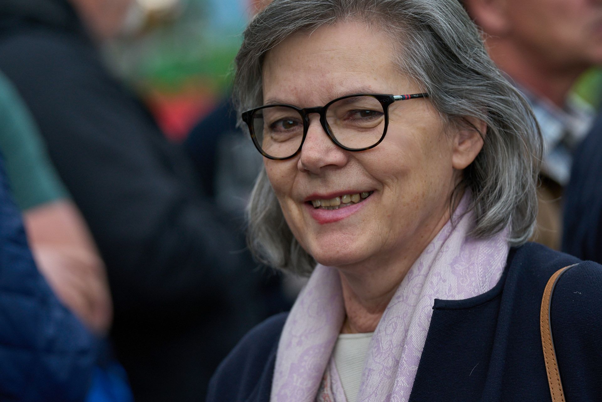 Eine Frau mit Brille und rosa Schal lächelt.