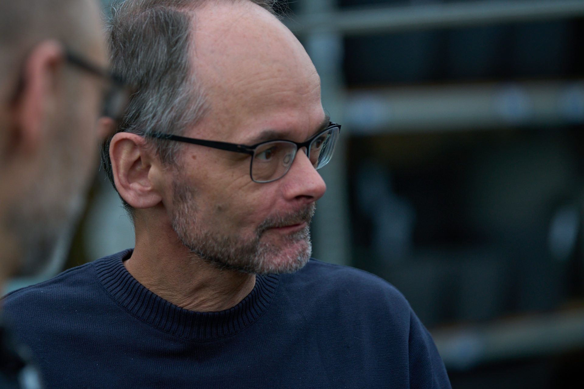 Ein Mann mit Brille und Bart spricht mit einem anderen Mann.