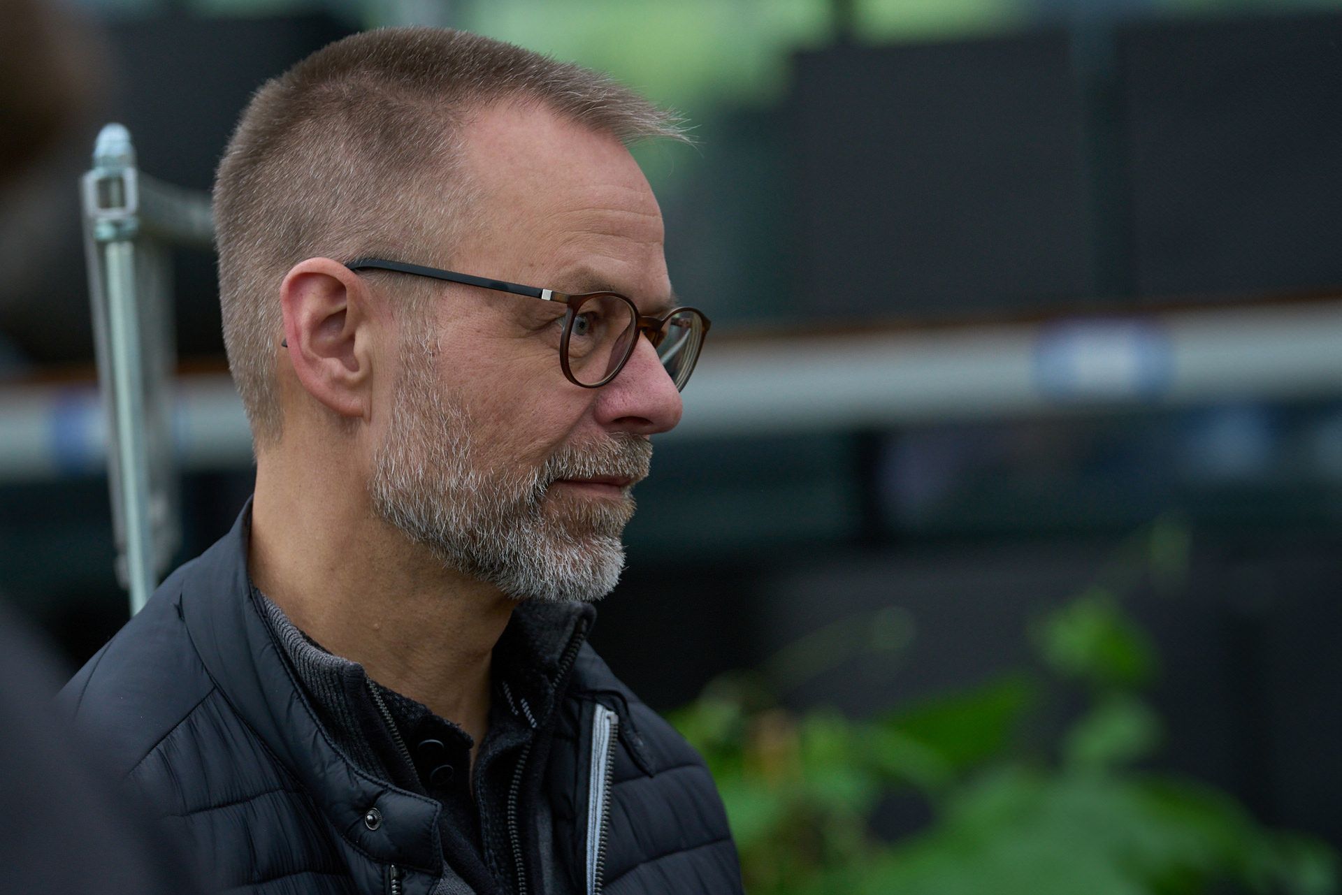 Ein Mann mit Bart und Brille trägt eine schwarze Jacke.