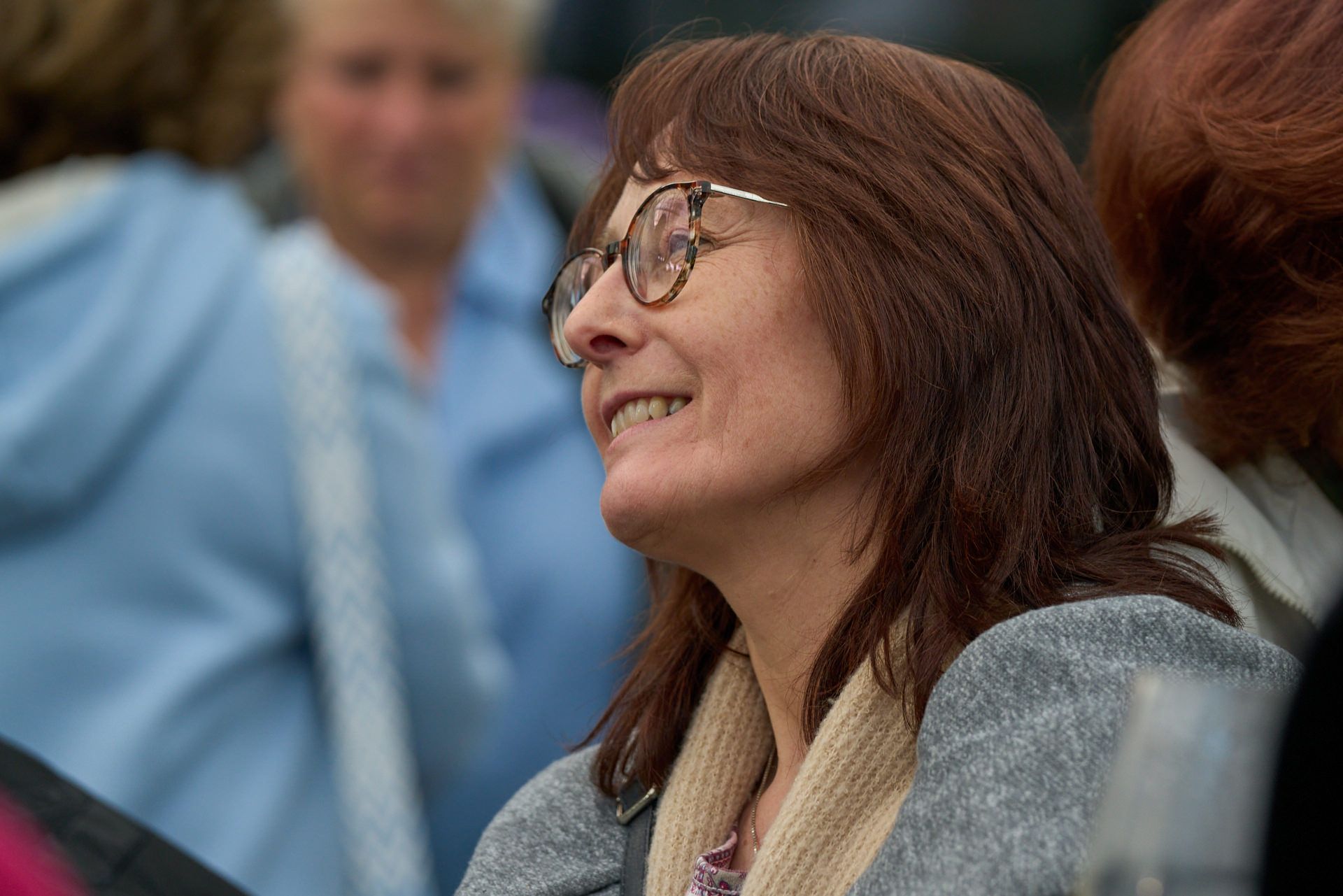 Eine Frau mit Brille lächelt in einer Menschenmenge.