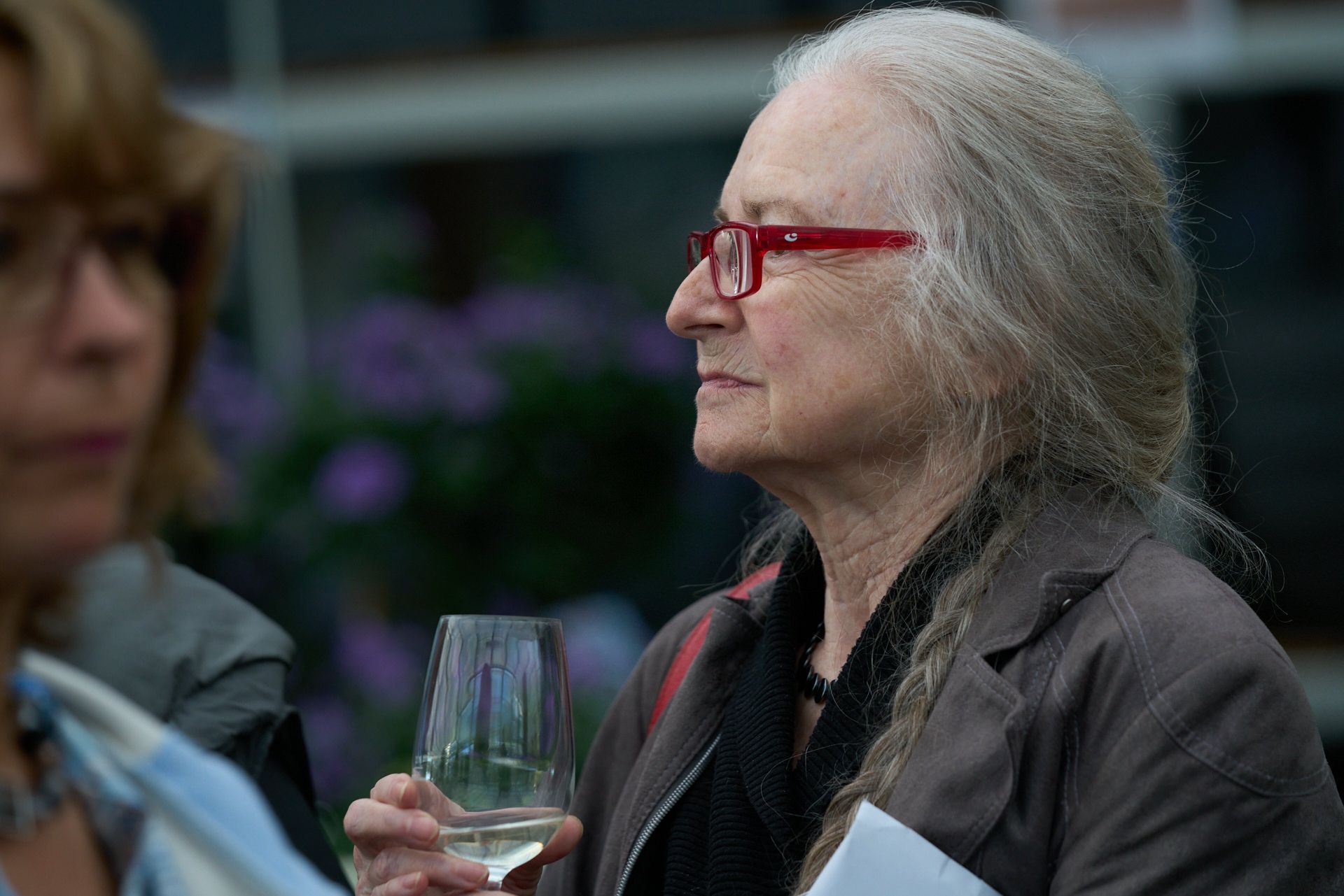 Eine Frau mit roter Brille hält ein Glas Wein.
