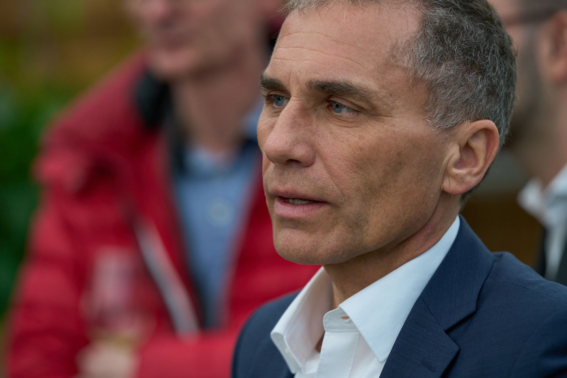 Ein Mann in Anzug und weißem Hemd sitzt in einer Menschenmenge.