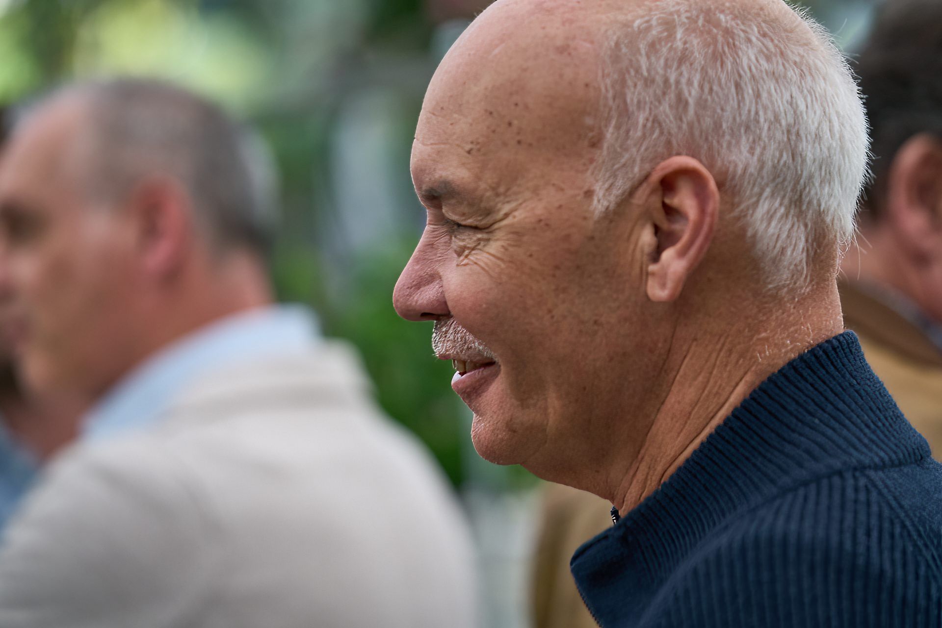 Ein Mann mit weißem Haar lächelt auf einem unscharfen Foto.