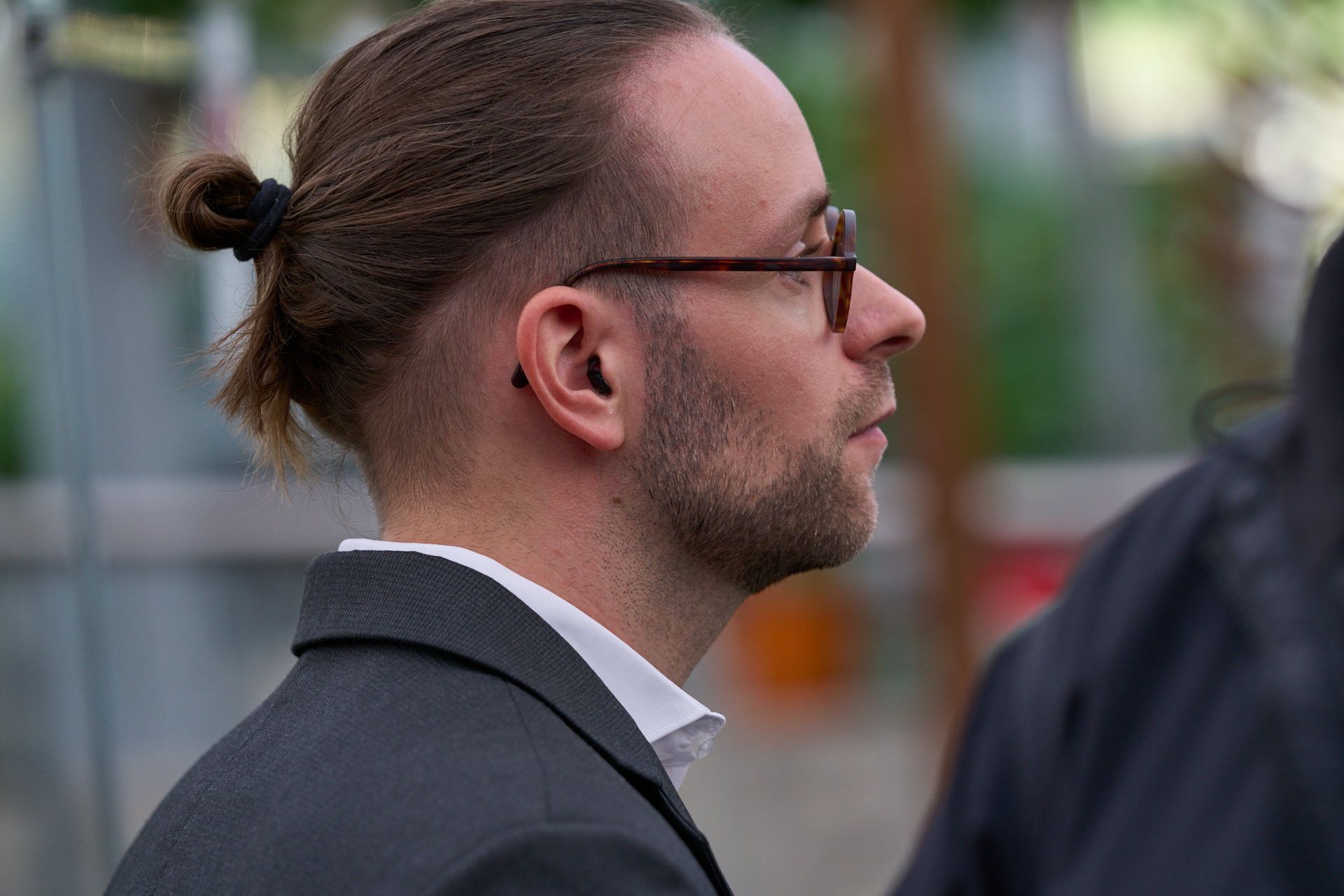 Ein Mann mit Pferdeschwanz und Brille trägt einen Anzug.