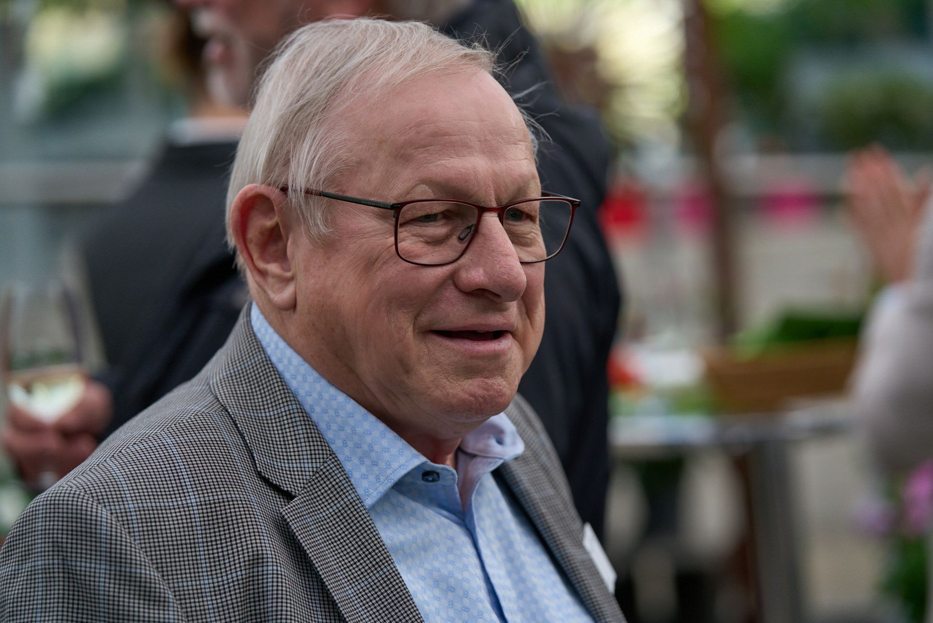 Ein älterer Mann mit Brille und Anzug lächelt.