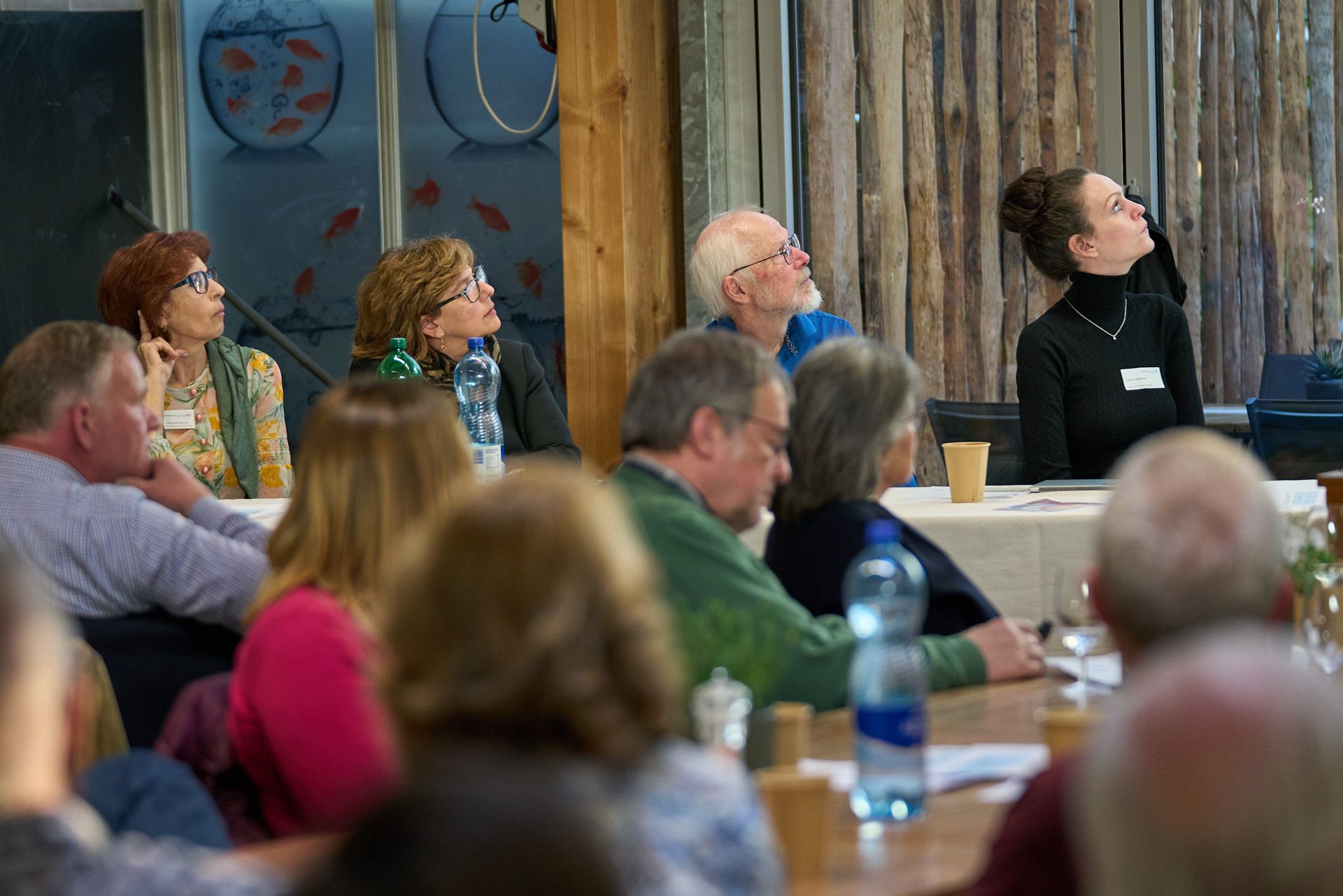 Eine Gruppe von Leuten sitzt an einem Tisch und hört sich eine Präsentation an.
