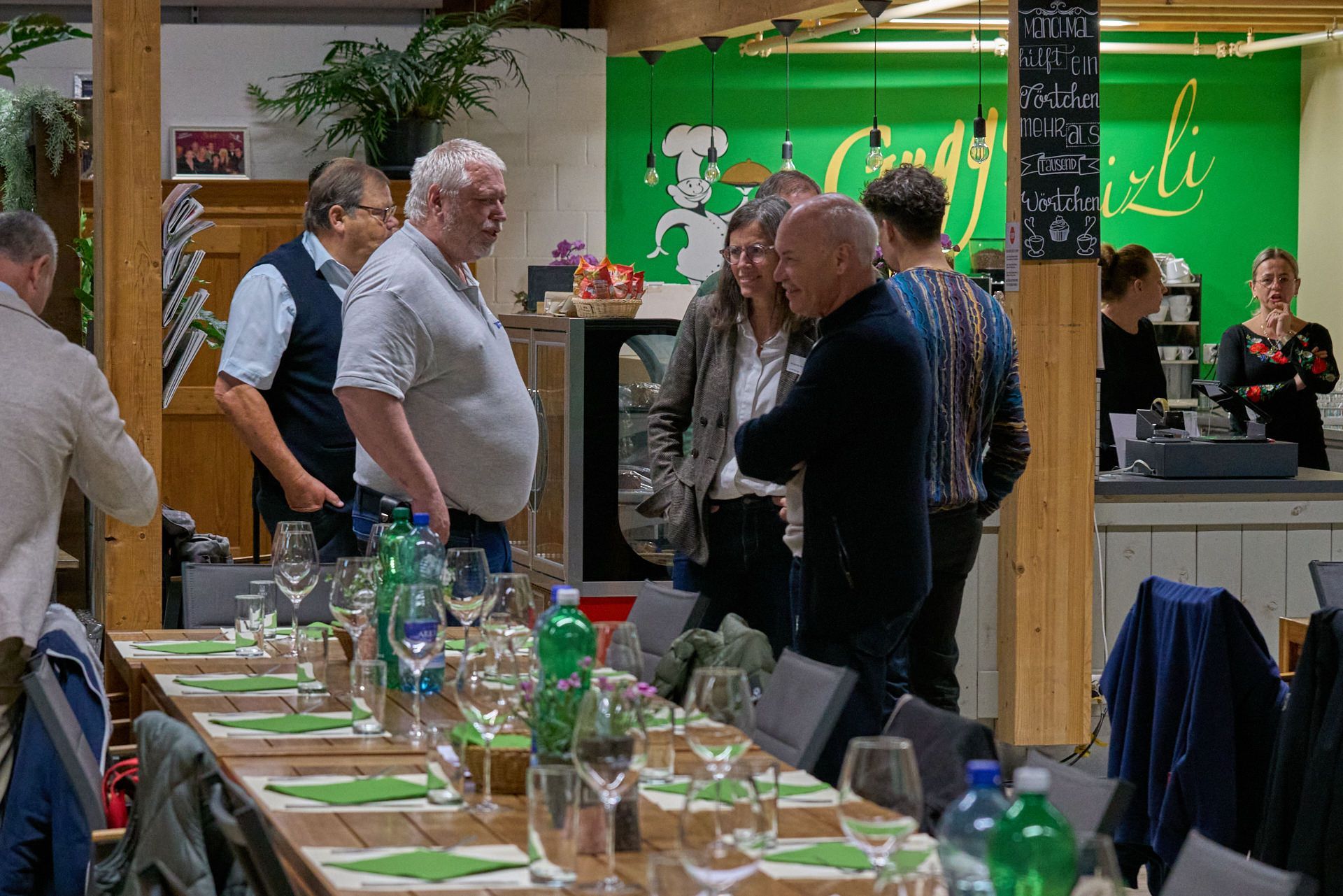 Eine Gruppe von Menschen steht in einem Restaurant um einen langen Tisch.