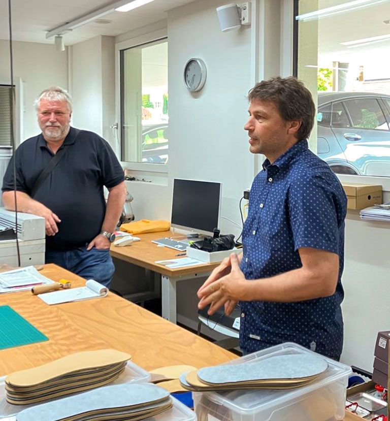 In einem Raum stehen zwei Männer um einen Tisch herum , auf dem ein Computer steht.