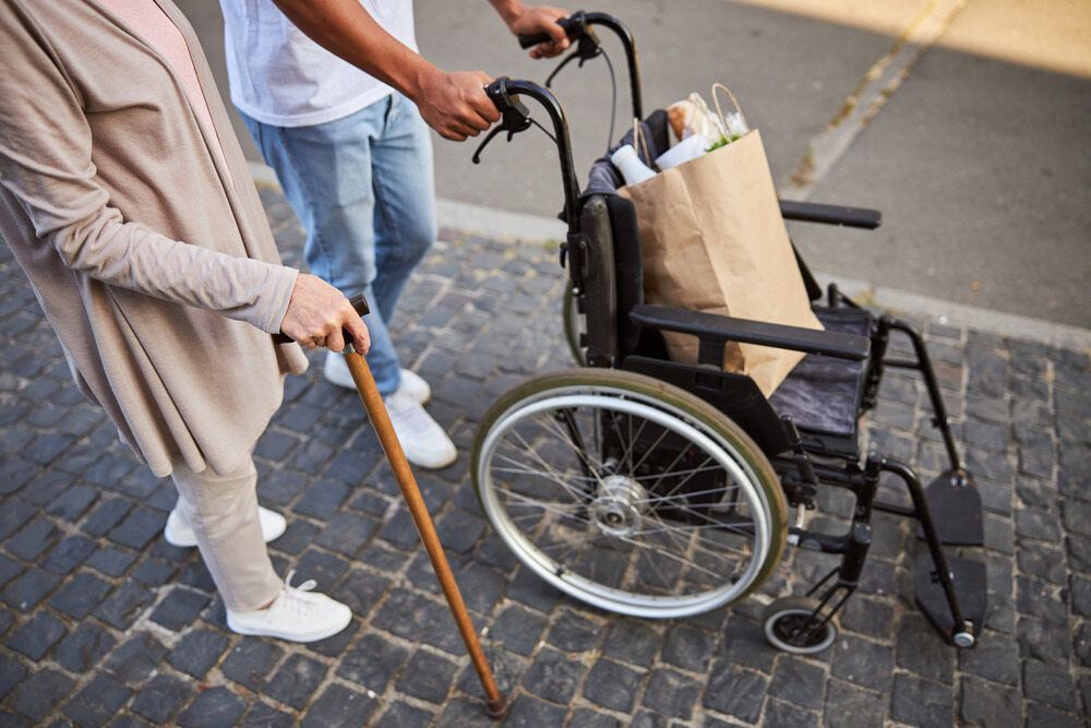 A Man is Pushing a Wheelchair — Empowering You Disability Services In Maryborough, QLD