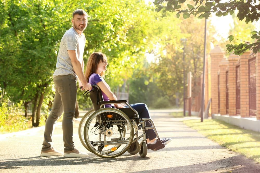 A Woman in a Wheelchair is Being Helped by a Man — Empowering You Disability Services In Maryborough, QLD