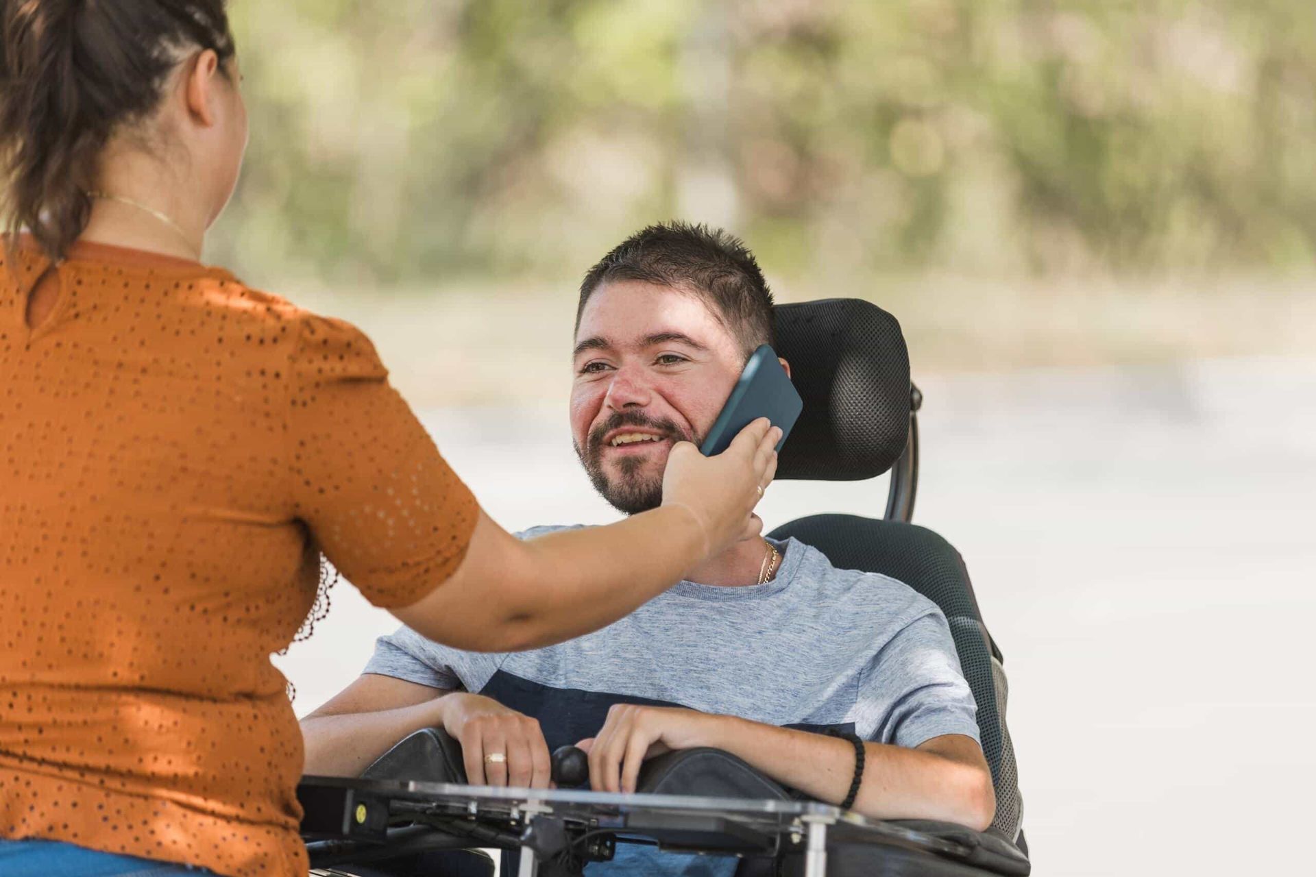 A Woman is Talking on a Cell Phone to a Man in a Wheelchair — Empowering You Disability Services In Maryborough, QLD