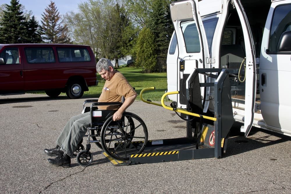 A Man in a Wheelchair is Being Lifted Into a Van  — Empowering You Disability Services In Maryborough, QLD