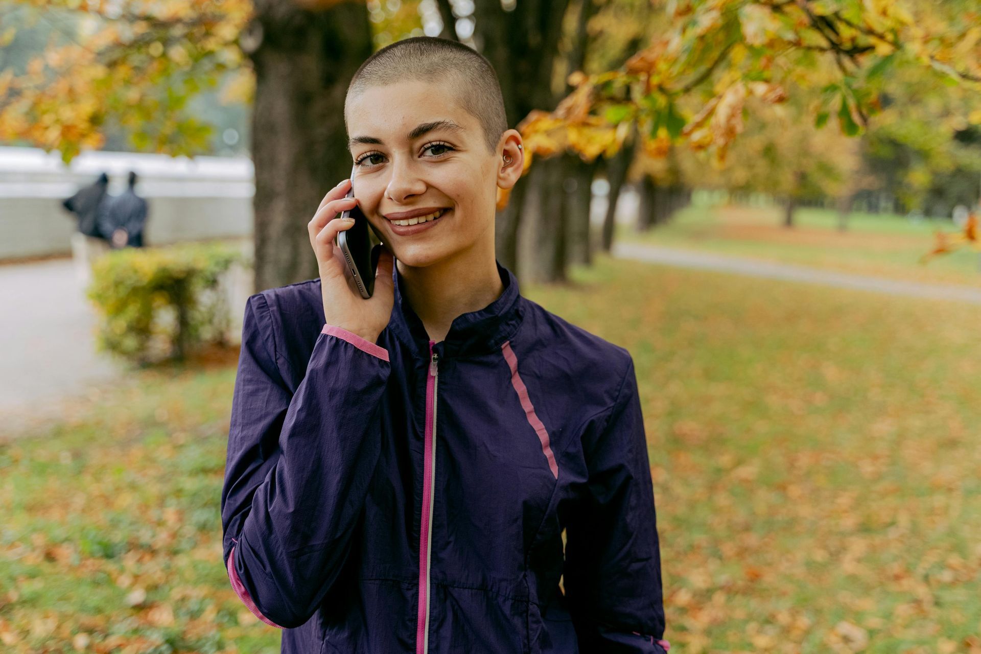 A Woman With a Shaved Head is Talking on a Cell Phone in a Park — Empowering You Disability Services In Maryborough, QLD