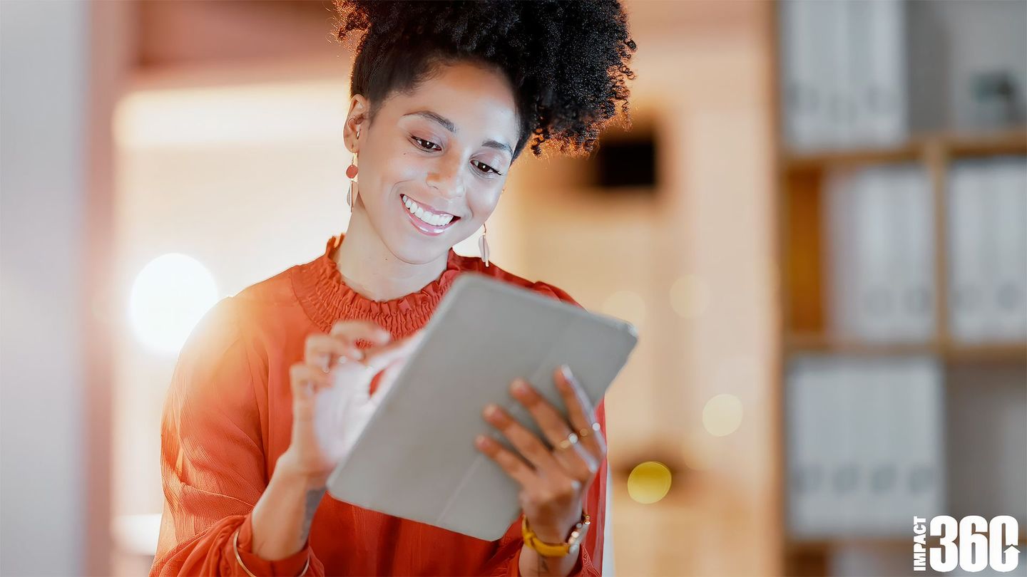 a woman is smiling while using a tablet with the impact 360 logo behind her