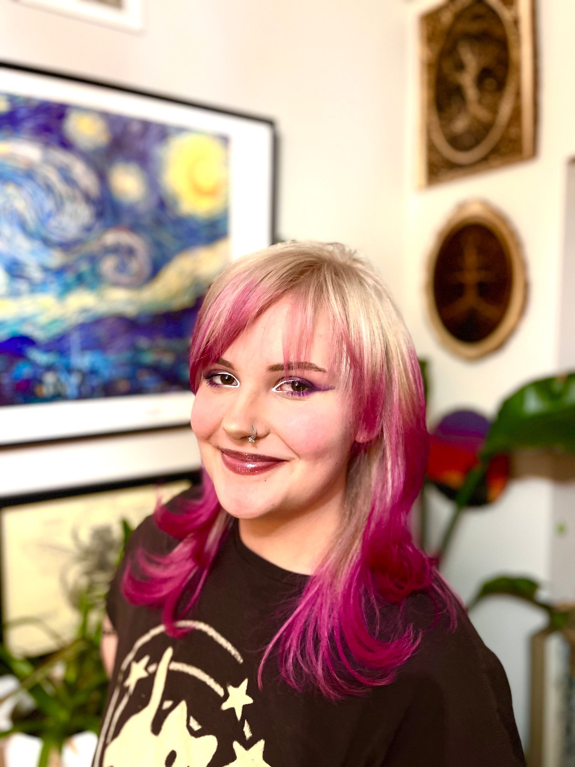 Woman with red hair, smiling, wearing a burgundy top and patterned cardigan, leaning against a colorful mural.